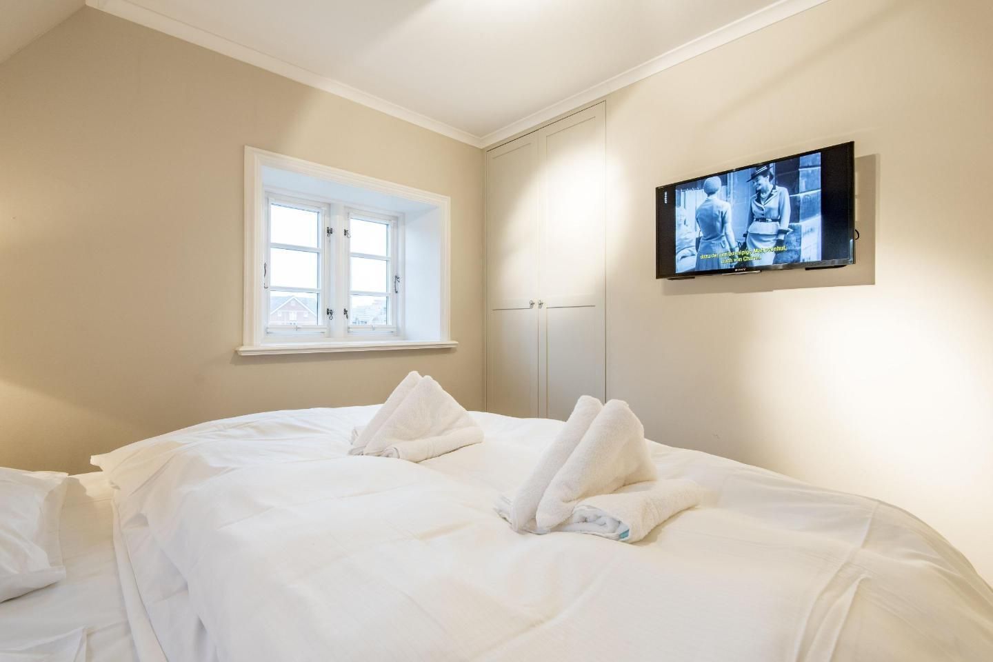 A hotel room with a bed, a television on the wall, and a window.