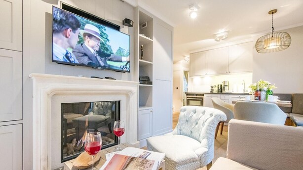 Un salon moderne doté d’une cheminée, d’un téléviseur fixé au mur et d’un coin repas visible à travers une porte ouverte.