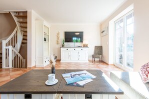Un salon spacieux avec une table basse en bois, un canapé blanc, un téléviseur et une grande fenêtre.