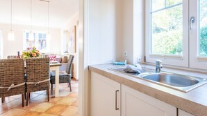 Une cuisine moderne dotée d’une grande fenêtre, d’un coin repas avec des chaises en osier et d’un évier.
