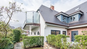 Une maison moderne dotée d’un balcon en verre, d’un chemin en pierre et d’un espace vert bien entretenu.