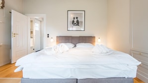 Un lit bien fait, avec du linge de lit blanc, une tête de lit grise et deux lampes de chevet.