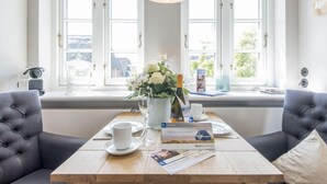 Een kamer met een houten tafel gedekt voor twee personen, een vaas met bloemen, een fles wijn en een welkomstfolder.