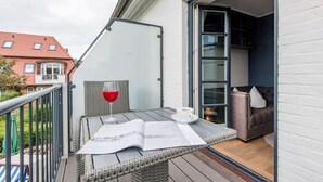 Een balkon met een rieten tafeltje, een glas rode wijn en een witte kop.
