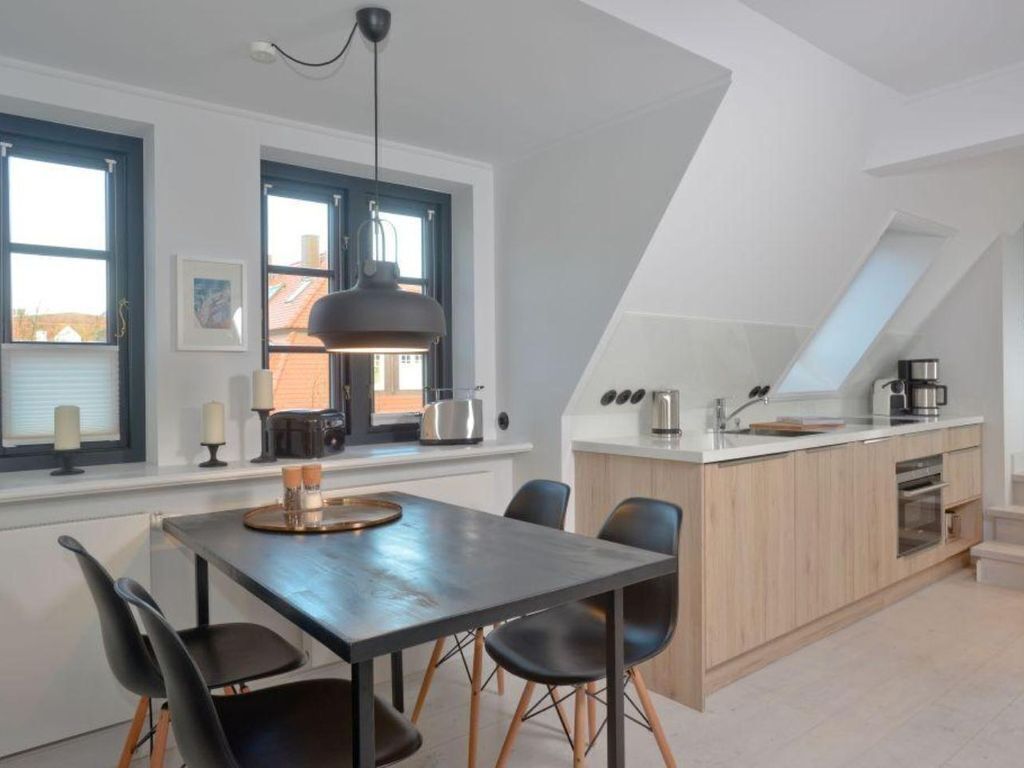 Eine moderne Küche mit Essbereich, inklusive einer großen Kücheninsel, Pendelleuchten und Blick auf die Stadt durch die Fenster.