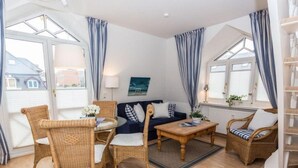 Een gezellige woonkamer met rieten meubels, een ronde salontafel en een bank met blauwe kussens.
