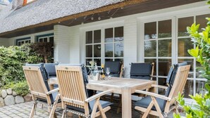A patio with a wooden table and chairs, a bottle of wine, and a glass. - House Süderhof, Seagull Whg. 13 - House Süderhof (Sylt-Ost)