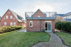 Ein zweistöckiges Haus mit Ziegelverkleidung, einem Balkon und einem gepflasterten Auffahrt.