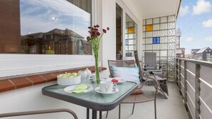 Ein Balkon mit Frühstückstisch, Blumen in einer Vase und Blick auf die Stadtlandschaft.