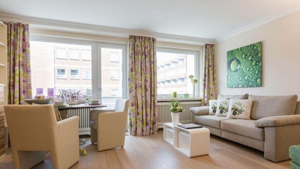 Ein modernes Wohnzimmer mit einer Couch, zwei Sesseln, einem Couchtisch und einem Essbereich mit Tisch für zwei Personen.
