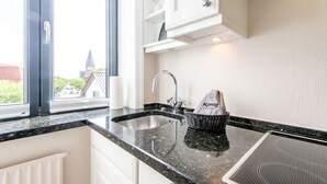Una cocina moderna con encimera de granito, pileta de acero inoxidable y muebles de cocina blancos. Una cesta con una bolsa etiquetada “König” está sobre la encimera.