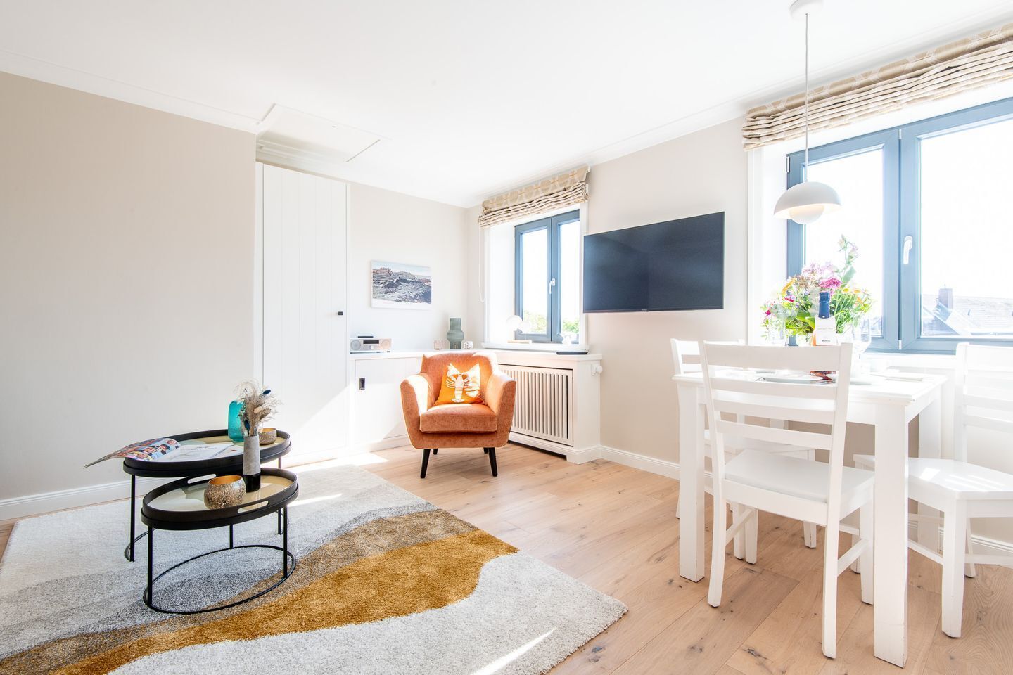 Ein helles Wohnzimmer mit einem weißen Sofa, einem runden Couchtisch und einem Essbereich mit weißen Stühlen und einem Tisch.