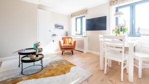 A bright living room with a white sofa, a round coffee table, and a dining area with white chairs and a table.