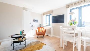 Ein helles Wohnzimmer mit einem weißen Sofa, einem runden Couchtisch und einem Essbereich mit weißen Stühlen und einem Tisch.