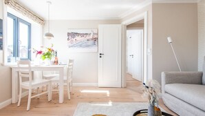 A bright living room with a dining area, a grey sofa, a white table, and a painting on the wall.