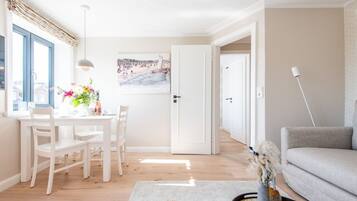 Ein helles Wohnzimmer mit Essbereich, einem grauen Sofa, einem weißen Tisch und einem Gemälde an der Wand.