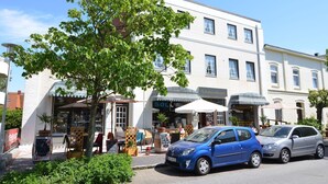 A street view with a white building, a tree, and parked cars.