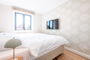 Une chambre à coucher avec un lit, un téléviseur fixé au mur et une fenêtre donnant sur l’extérieur.