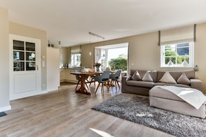 A spacious living area with a wooden floor, a grey sofa, and a dining table with chairs.