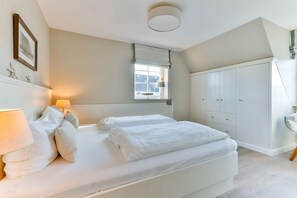 A bedroom with a bed, bedside lamps, a window, and a wardrobe.
