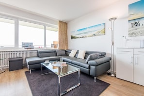 A modern living room with a grey leather sofa, a glass coffee table, and a painting of a landscape. - Meerblick. Strand. Gemütlich. - Objekt-id: Dkw/98 - Dünenhof zum Kronprinzen (Wenningstedt-Braderup (Sylt))