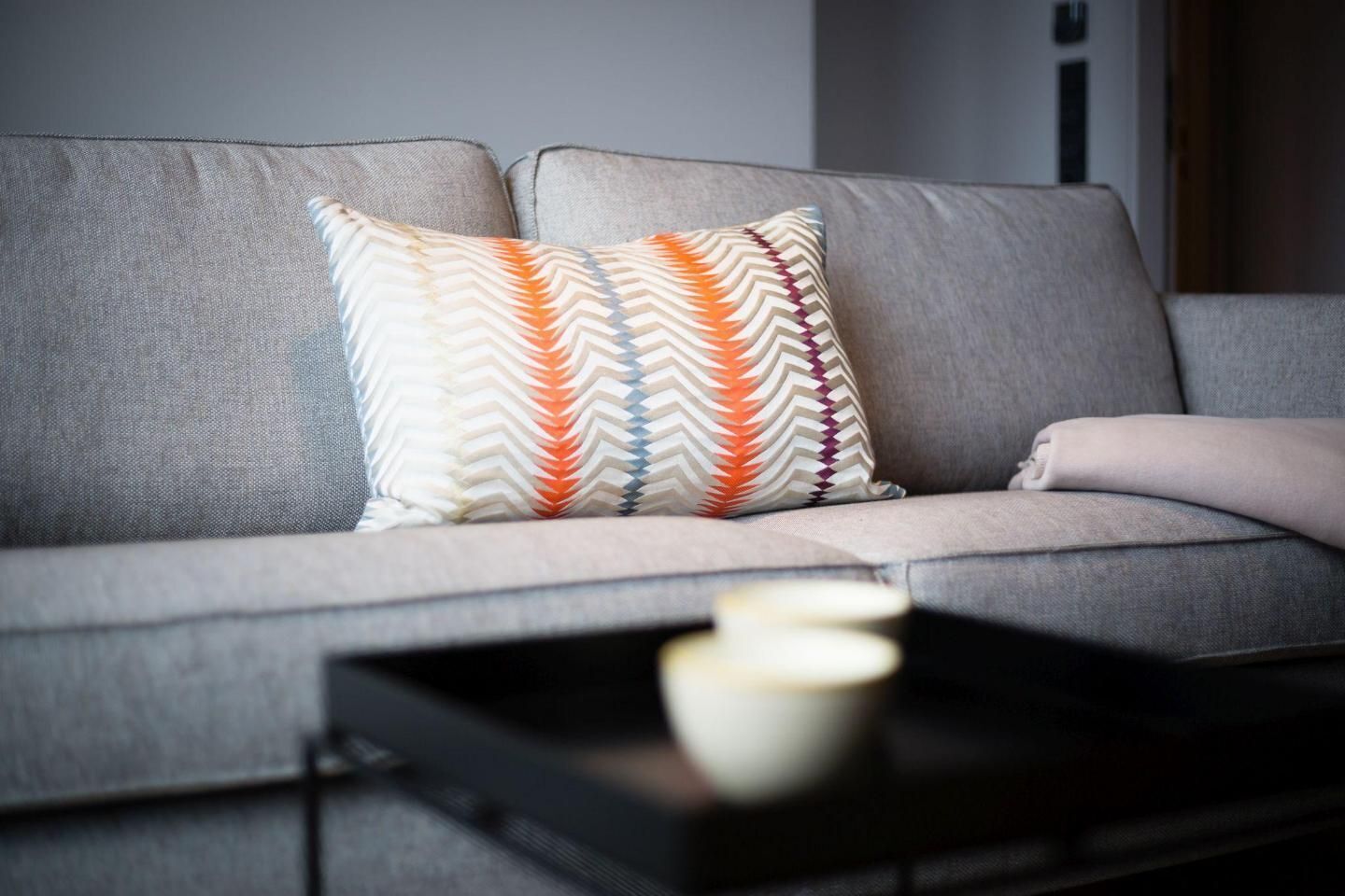 Ein graues Sofa mit zwei gemusterten Kissen und einer weißen Kerze auf einem schwarzen Tablett.