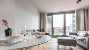A modern living room with a dining area, large windows, and a view of buildings outside.