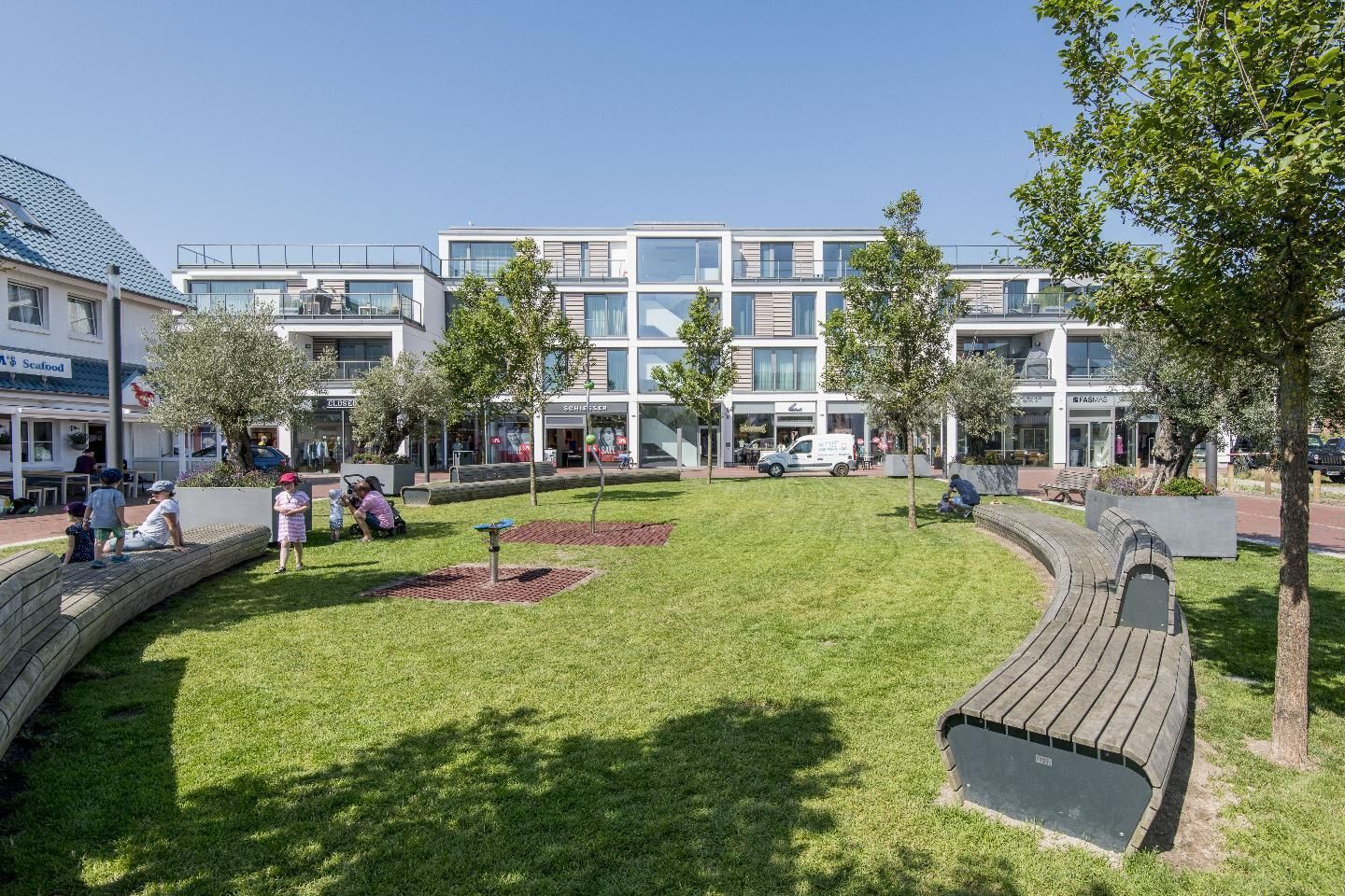 A modern building with multiple floors, a grassy courtyard, and a wooden bench.
