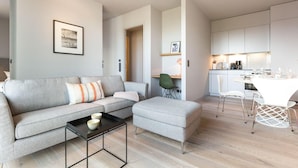 A modern living room with a grey sofa, a small coffee table, and a dining area with white chairs and a table.