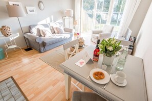 A modern living room with a sofa, dining table, and a view of the garden. - Modern. Bright. Central. - House Friesische Straße (Sylt)