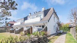 Une maison à deux étages, avec un toit en pente, un mur en pierre et une clôture en bois.