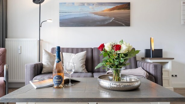 Une pièce avec un canapé, une table sur laquelle se trouvent une bouteille, un verre et un vase de fleurs.