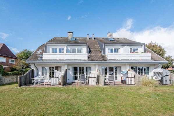 A two-story house with a large front lawn, multiple windows, and a covered patio area with outdoor furniture.