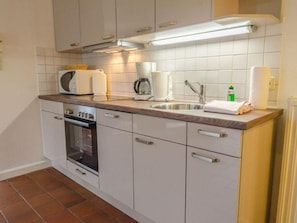 A modern kitchen with white cabinets, a built-in oven, a microwave, a coffee maker, and a sink.