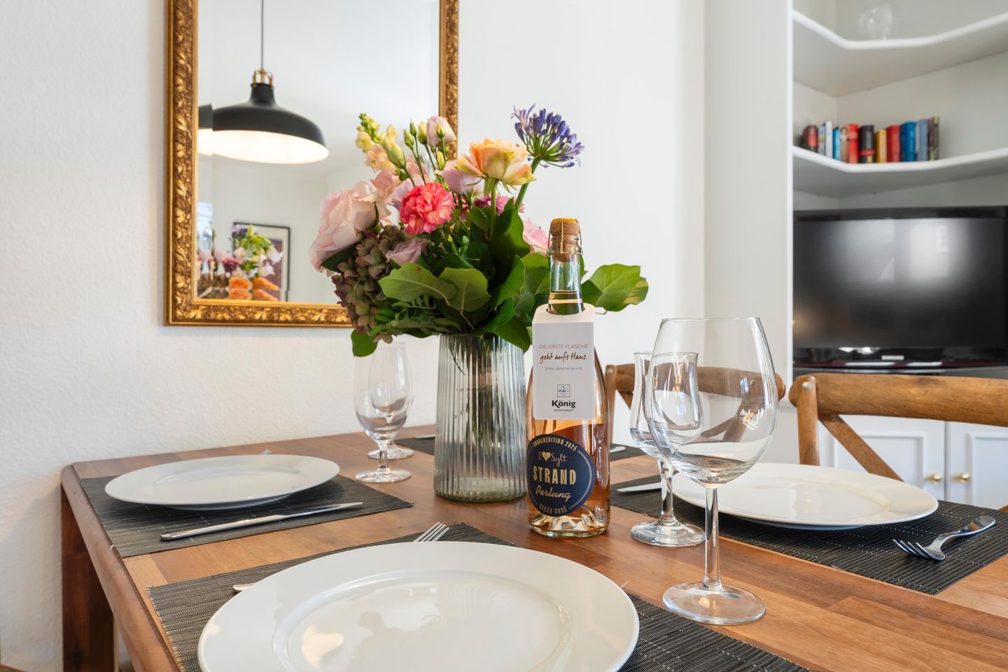 A dining table set with plates, wine glasses, a bottle of wine, and a vase of flowers.
