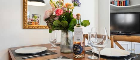 A dining table set with plates, wine glasses, a bottle of wine, and a vase of flowers.