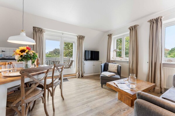A well-lit room with a dining table, chairs, a sofa, and a television.