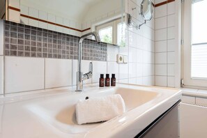 A bathroom with a white sink, chrome faucet, and a towel. There are three bottles on the counter.