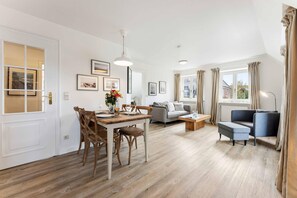 A modern living room with a dining area, a sofa, a coffee table, and a lamp. - Ruhe. Balkon. Gemütlich. - Senwai-hüs, Whg. 3 "morsum" - Objekt-id: Hsw/03 - Senwai-hüs (Sylt)