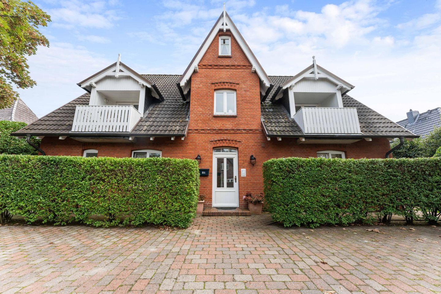 A two-story house with a central entrance, a balcony on the upper floor, and a brick facade.