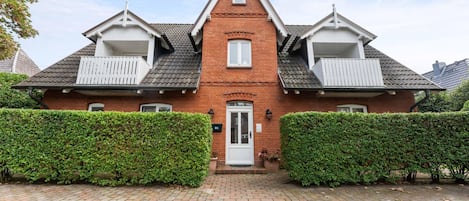 A two-story house with a central entrance, a balcony on the upper floor, and a brick facade.