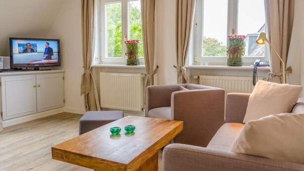 A living room with a wooden coffee table, beige sofa, and a television on a white cabinet. - Ruhe. Balkon. Gemütlich. - Senwai-hüs, Whg. 3 "morsum" - Objekt-id: Hsw/03 - Senwai-hüs (Sylt)