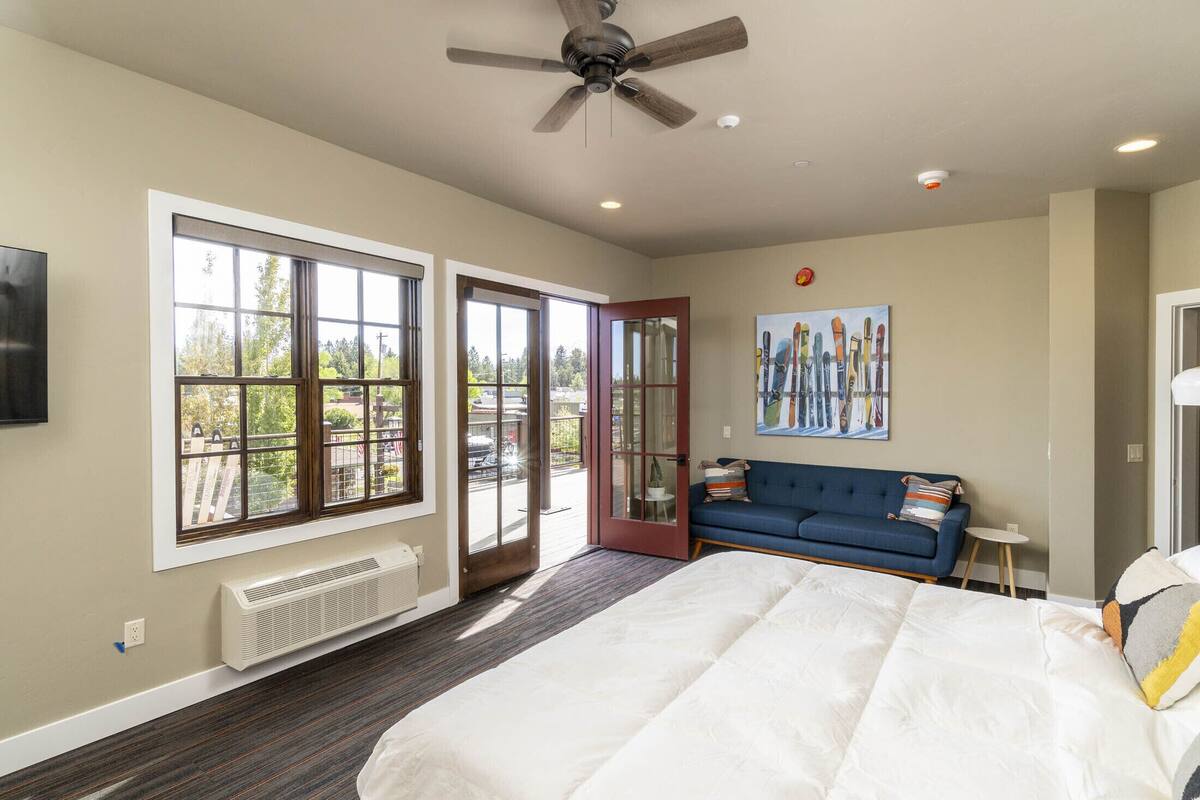 A bedroom with a large bed, a ceiling fan, a blue sofa, and a painting on the wall.