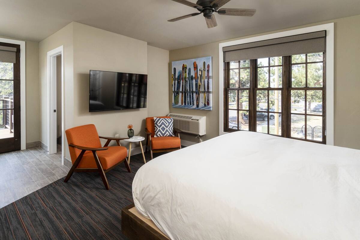 A hotel room with a large bed, two chairs, a TV, and a painting of skis.