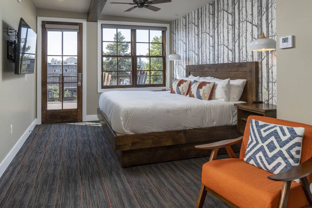 A bedroom with a large bed, a chair, a nightstand, a ceiling fan, and a view through a door.