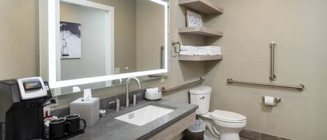 A modern bathroom with a large mirror, a coffee maker, a sink, and a toilet.