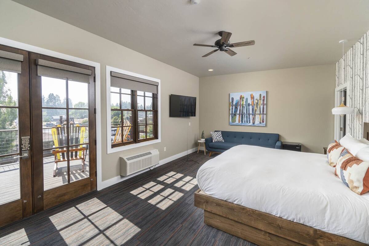 A bedroom with a large bed, a ceiling fan, a TV, and a view of the outdoors through a sliding door.