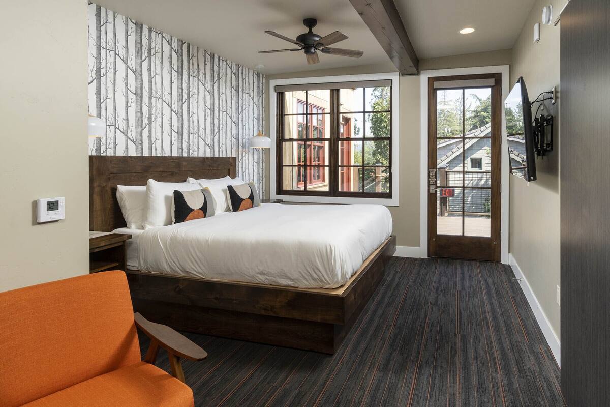 A bedroom with a large bed, a wooden headboard, a ceiling fan, a window with a view, and a TV mounted on the wall.