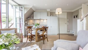 A modern kitchen with white cabinets, a dining area with wooden chairs, and a large window providing natural light. - Exquisit. Wellness. Modern. - Objekt-id: Hm/05 - Haus Magnus (Sylt)