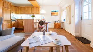 Un salón acogedor con un sofá, una mesita de centro con una vela, y vistas a la cocina y al comedor.